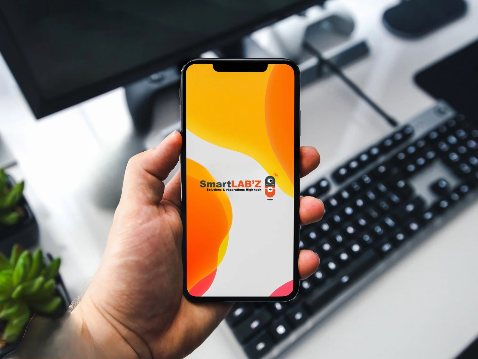 Un smartphone tenu en main devant un bureau, l'écran d'accueil aux couleurs de SmartLAB'Z